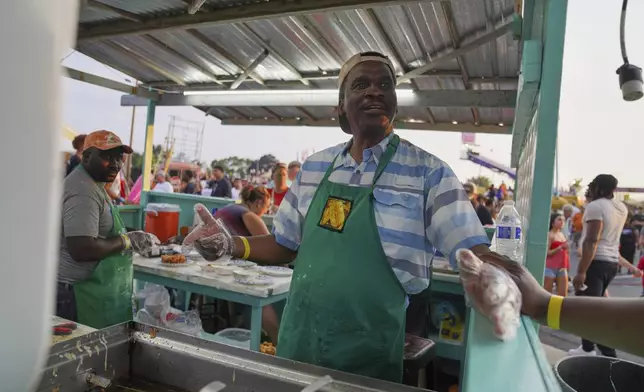 Bienvenue D'Almeida, who applied for and won the so-called green card lottery, a program for countries with low rates of emigration to the United States, makes funnel cake and deep-fried Snickers bars at the St. Jude Catholic Church's Sweet Corn Festival on Saturday, Aug. 9, 2025, in Cedar Rapids, Iowa. (AP Photo/Jessie Wardarski)