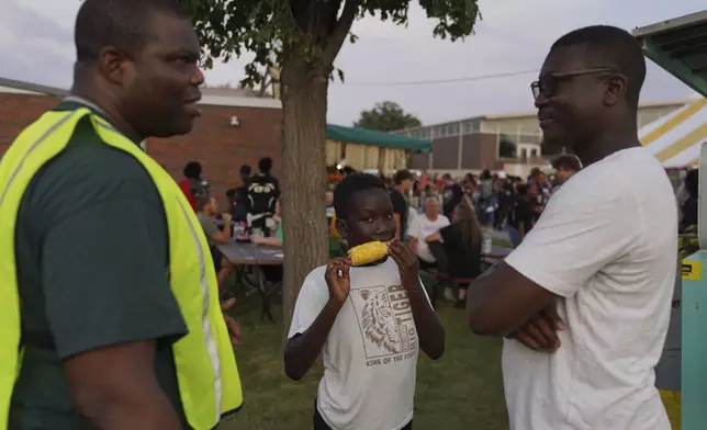 Samy Yawo, center, eats sweet corn at the St. Jude Catholic Church's Sweet Corn Festival as his father, Billy Yawo, right, talks with, Roger Atchou, left, a father of two from Togo, on Saturday, Aug. 9, 2025, in Cedar Rapids, Iowa. (AP Photo/Jessie Wardarski)