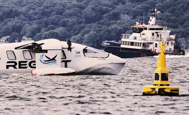 The REGENT Viceroy Seaglider, a winged passenger ferry, passes a navigation buoy and a ship during a test run on Narragansett Bay, Wednesday, Aug. 6, 2025, off the coast of North Kingstown, R.I. (AP Photo/Charles Krupa)