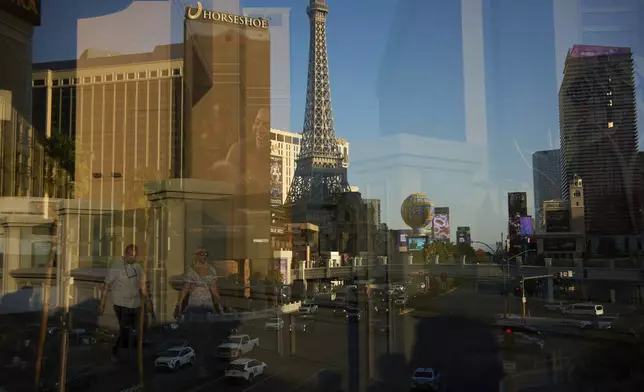 Reflected in a glass window, people walk across a pedestrian bridge along the Las Vegas Strip, Friday, Aug. 8, 2025, in Las Vegas. (AP Photo/John Locher)