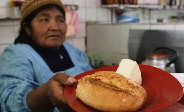 A vendor gives "pan de batalla," or battle bread, which is made with government subsidized flour, to a client at a restaurant in La Paz, Bolivia, Saturday, Aug. 9, 2025. (AP Photo/Juan Karita)