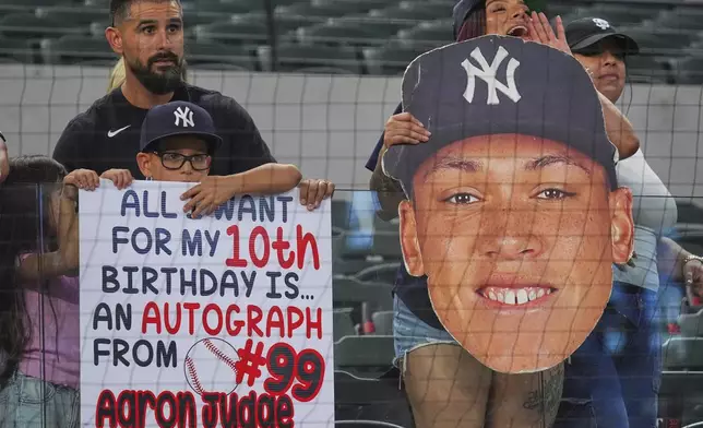 Fans in the stands hold signs before a baseball game between the New York Yankees and the Texas Rangers, Monday, Aug. 4, 2025, in Arlington, Texas. (AP Photo/LM Otero)