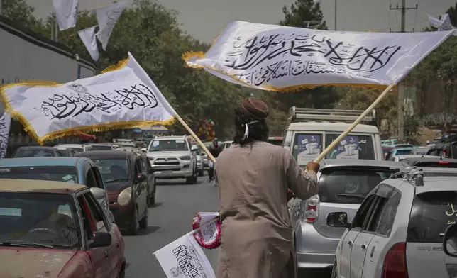 A man waves Taliban flags for sale amid traffic ahead of celebrations marking the fourth anniversary of the U.S. withdrawal from Afghanistan and the start of Taliban rule in Kabul, Afghanistan, Thursday, Aug. 14, 2025. (AP Photo/Siddiqullah Alizai)