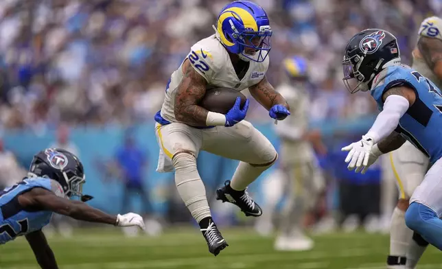 Los Angeles Rams running back Blake Corum, center, runs the ball as Tennessee Titans cornerback Jarvis Brownlee Jr., left, and safety Amani Hooker defend during the second half of an NFL football game Sunday, Sept. 14, 2025, in Nashville, Tenn. (AP Photo/George Walker IV)