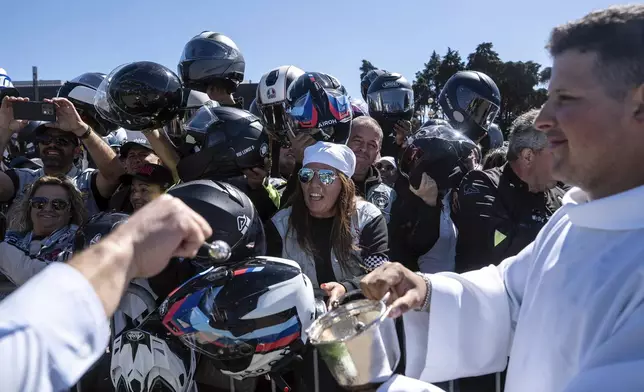 A priest blesses motorcyclists' helmets during the 10th Pilgrimage of the Blessing of Helmets that draws tens of thousands, at the Roman Catholic holy shrine of Fatima, in Fatima, Portugal, Sunday, Sept. 21, 2025. (AP Photo/Ana Brigida)