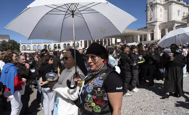 A motorcyclist holds an umbrella for nun carrying a communion wafer box at the Roman Catholic holy shrine of Fatima, during the 10th Pilgrimage of the Blessing of Helmets that draws tens of thousands, in Fatima, Portugal, Sunday, Sept. 21, 2025. (AP Photo/Ana Brigida)