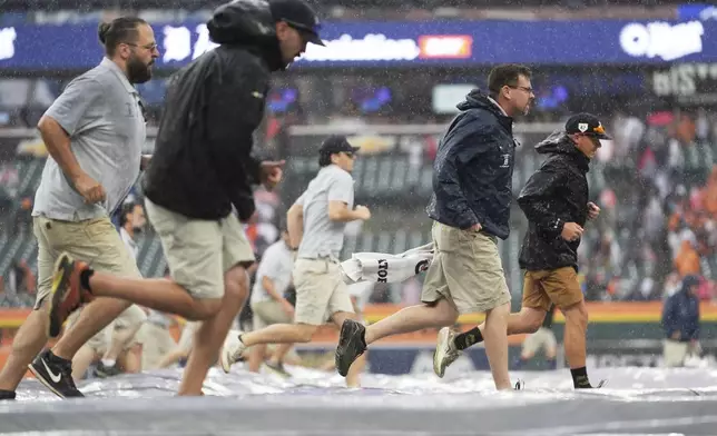 Groundskeepers roll out a tarp during a weather delay during the seventh inning of a baseball game between the Detroit Tigers and the Atlanta Braves, Sunday, Sept. 21, 2025, in Detroit. (AP Photo/Ryan Sun)