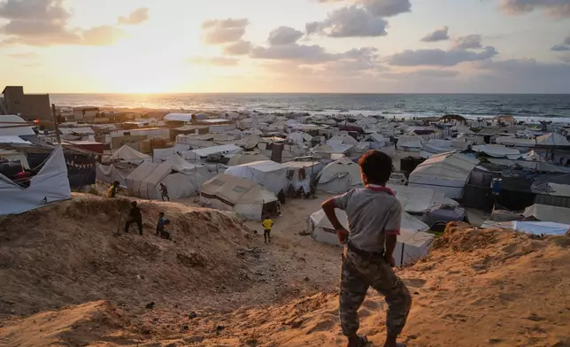 Displaced Palestinians walk through a tent camp in Muwasi, an area that Israel has designated as a safe zone, in Khan Younis southern Gaza Strip, Thursday, Sept. 25, 2025. (AP Photo/Jehad Alshrafi)
