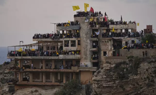 Hezbollah supporters stand on building to watch the landmark Raouche sea rock which illuminated by a portrait of late Hezbollah leader Sayyed Hassan Nasrallah during an event commemorating his anniversary assassination, in Beirut, Lebanon, Thursday, Sept. 25, 2025. (AP Photo/Hussein Malla)