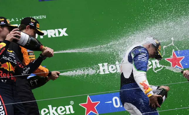 Red Bull driver Max Verstappen of the Netherlands, left, and McLaren driver Oscar Piastri of Australia spray Racing Bulls driver Isack Hadjar of France with champagne as they celebrate on the podium after the Formula One Dutch Grand Prix race at the Zandvoort racetrack in Zandvoort, Netherlands, Sunday, Aug. 31, 2025. (AP Photo/Patrick Post)
