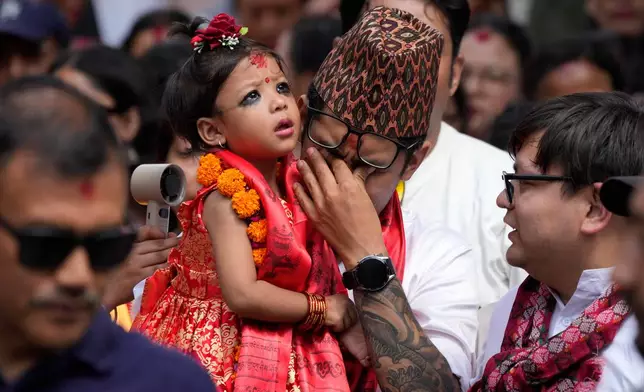 Nepal's newly appointed living goddess, Kumari Aryatara Shakya, is carried by her father as they walk towards Kumari Ghar, the temple palace where she will be residing in Kathmandu, Nepal, Tuesday, Sept. 30, 2025. (AP Photo/Niranjan Shrestha)