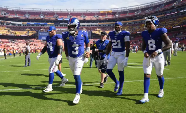 Walking off the field at the end of an NFL football game are from l-r., New York Giants guard Greg Van Roten (74), quarterback Russell Wilson (3), cornerback Paulson Adebo (21) and safety Jevon Holland (8), Sunday, Sept. 7, 2025, in Landover, Md. Commanders won 21-6. (AP Photo/Stephanie Scarbrough)