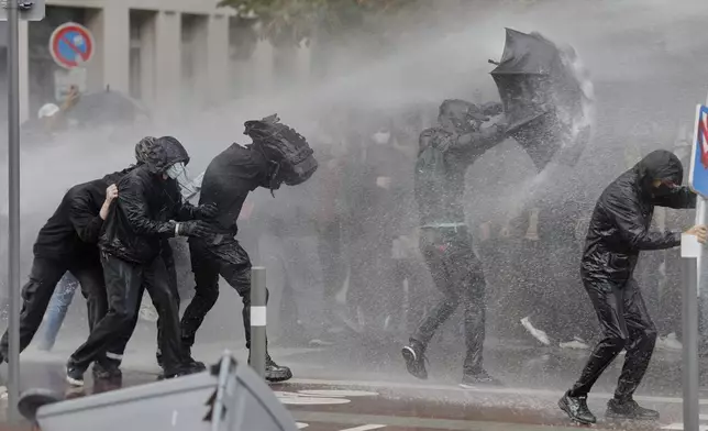Protesters of the "Block Everything" movement take cover from a spraying water canon in Lille, northern France, Wednesday, Sept. 10, 2025. (AP Photo/Jean-Francois Badias)
