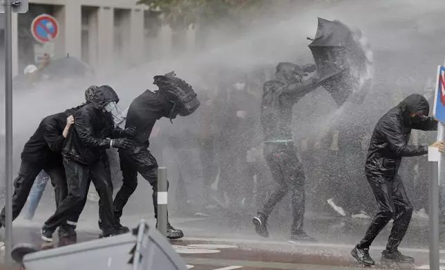 A protesters of the "Block Everything" movement takes cover of a water canon behind an umbrella in Lille, northern France, Wednesday, Sept. 10, 2025. (AP Photo/Jean-Francois Badias)