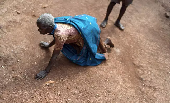 Saverina Tumukunde, 67, who struggles with mental illness, chases ants on the ground outside her home as her husband Daniel Nvunabandi, 75, right, looks on, Wednesday, Nov. 20, 2024, in Omukayaga, a rural village in western Uganda. Older people living in rural villages with dementia and mental illness, conditions so foreign to many here, have been accused of witchcraft and ostracized in their own communities. (AP Photo/David Goldman)