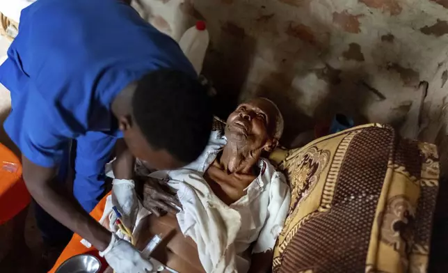 Field nurse Derrick Ssemanda, left, with Reach One Touch One Ministries, changes the catheter of Yafesi Nakyanga, 86, during a visit to his home, Saturday, Nov. 16, 2024, in Nabalanga, Uganda. (AP Photo/David Goldman)