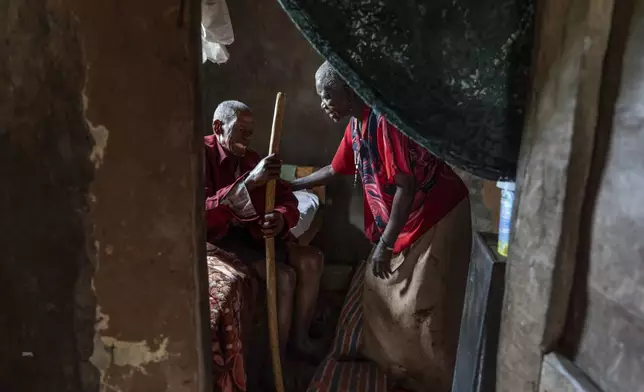 Erisafan Khayiki, 80, whose feet are so swollen they hurt just to place them on the floor, grimaces in pain as he tries to get out of bed with the help of his wife, Maria Kimono, 69, at their home in Nabalanga, Uganda, Saturday, Nov. 16, 2024. (AP Photo/David Goldman)