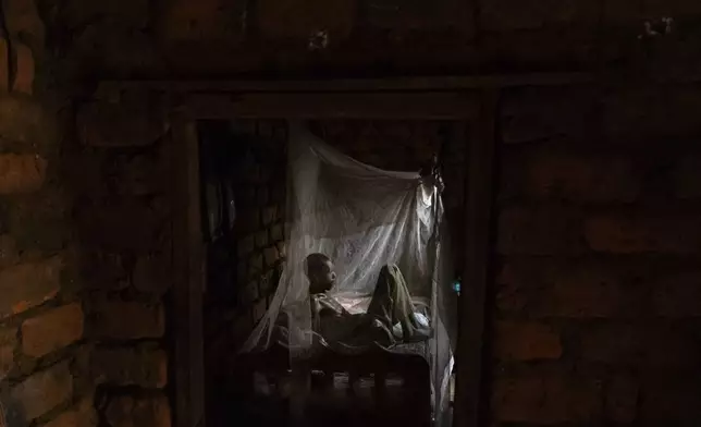 Joseph Malagho, who is about 70 and has survived living with HIV but now faces the complexities of old age, sits in his bed under a mosquito net at his home in Nkulagirire, Uganda, Friday, Nov. 15, 2024. (AP Photo/David Goldman)