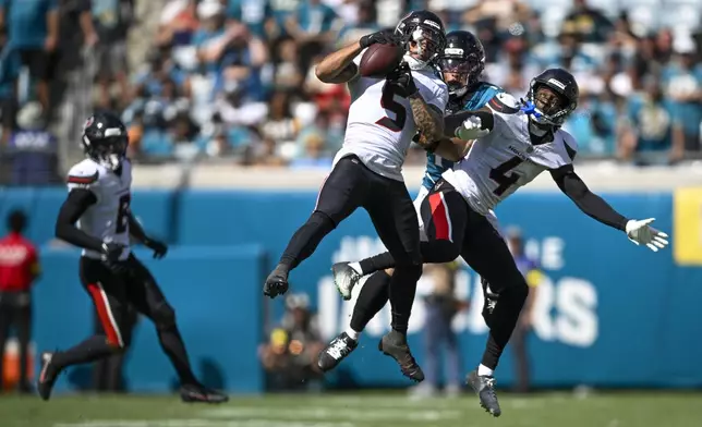 Houston Texans safety Jalen Pitre (5) intercepts a pass intended for Jacksonville Jaguars wide receiver Parker Washington, center, as teammate cornerback Kamari Lassiter (4) helps defend during the second half of an NFL football game Sunday, Sept. 21, 2025, in Jacksonville, Fla. (AP Photo/Phelan M. Ebenhack)