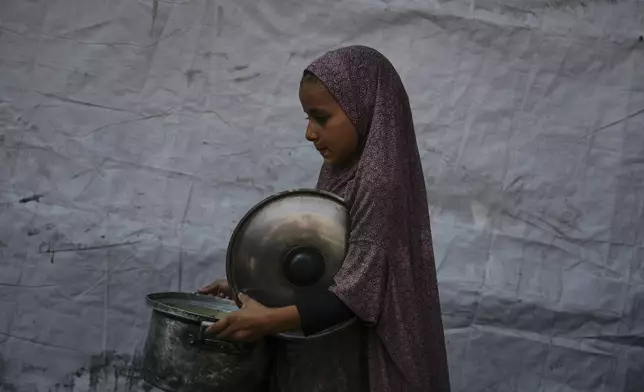 A Palestinian child carries a pot of donated food from a community kitchen in Deir al-Balah, southern Gaza Strip, Saturday, Sept. 6, 2025. (AP Photo/Jehad Alshrafi)