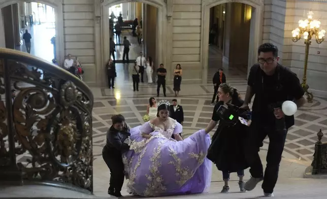 Leyla Portillo gets help with her gown from her mother Olga Portillo, left, and videographer-photographer Paola Soto, second from right, as Soto's husband and photographer Cesar Lopez, far right, walks ahead during her quinceañera portrait session at City Hall in San Francisco, Monday, April 28, 2025. (AP Photo/Jeff Chiu)