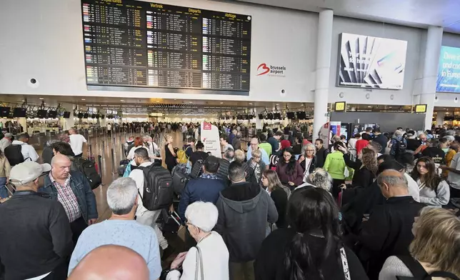 People stand in front of a departure board after a cyber attack caused delays at Brussels International Airport in Zaventem, Belgium, Saturday, Sept. 20, 2025. (AP Photo/Harry Nakos)