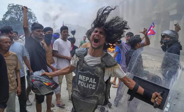 A protester wearing flak jacket and carrying a shield snatched from a policeman shouts slogans at the Singha Durbar, the seat of Nepal's government's various ministries and offices during a protest against social media ban and corruption in Kathmandu, Nepal, Tuesday, Sept. 9, 2025. (AP Photo/Niranjan Shrestha)