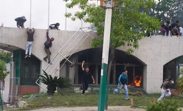 Protesters jump from a burning building during clashes with riot police in Kathmandu, Nepal, Monday, Sept. 8, 2025. (AP Photo/Niranjan Shrestha)