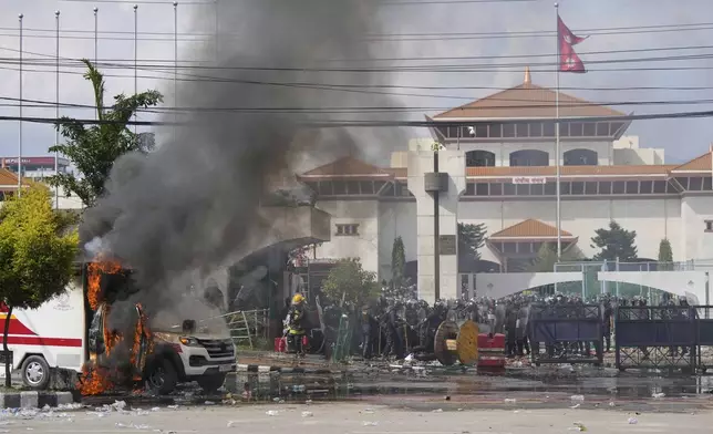 Riot police guard parliament building while an ambulance burns during protests in Kathmandu, Nepal, Monday, Sept. 8, 2025. (AP Photo/Niranjan Shrestha)