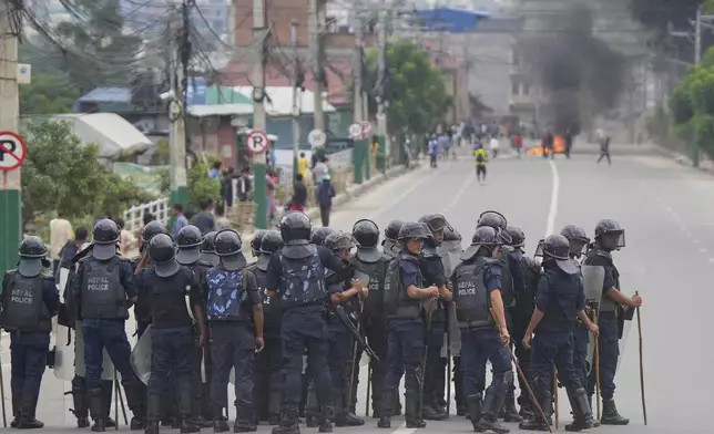 Policemen in riot gear stand guard on a street as protesters burn tires violating curfew orders in Kathmandu, Nepal, Tuesday, Sept. 9, 2025 after Nepal’s government lifted its ban on social media platforms after violent street protests. (AP Photo/Niranjan Shrestha)