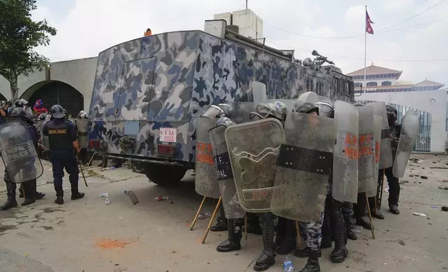 Riot police take cover behind an armored vehicle during clashes with protesters outside the Parliament building in Kathmandu, Nepal, Monday, Sept. 8, 2025. (AP Photo/Niranjan Shrestha)