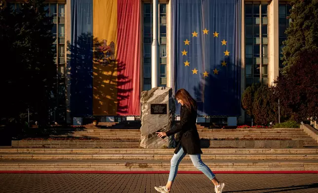 A woman runs in front of the government building, decorated with European Union and Moldovan flags in Chisinau, Moldova, Friday, Sept. 26, 2025, ahead of parliamentary elections taking place on Sept. 28. (AP Photo/Vadim Ghirda)