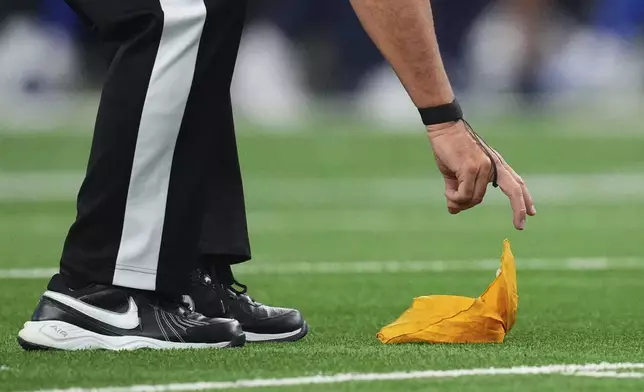 An official picks up a penalty flag in the first half of an NFL football game between the New York Giants and Dallas Cowboys Sunday, Sept. 14, 2025, in Arlington, Texas. (AP Photo/Julio Cortez)