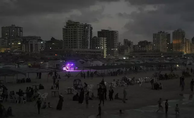 An illuminated food stand stands out as Palestinians cool off in the Mediterranean Sea at dusk near Gaza City's port, Tuesday, Sept. 2, 2025. (AP Photo/Jehad Alshrafi)
