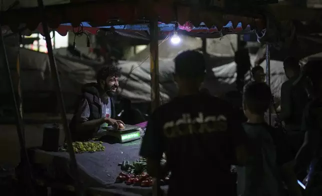 A Palestinian street vendor smiles at his customers as he sells vegetables near the beachfront at a tent camp for displaced people in the Gaza City port, Tuesday, Sept. 2, 2025. (AP Photo/Jehad Alshrafi)