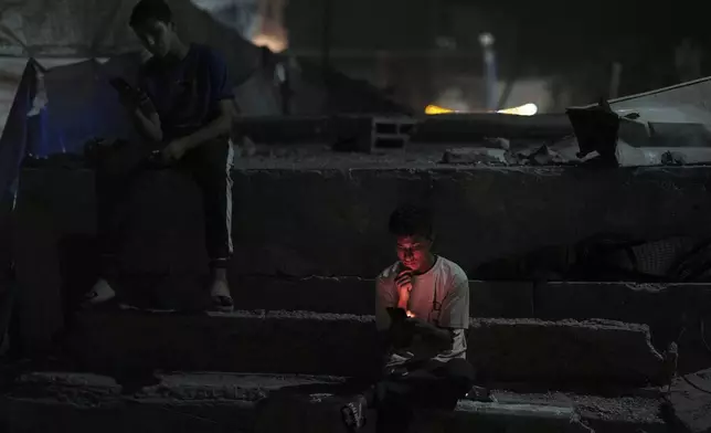 Palestinian youth check their phones as they stand on a street in the Gaza City, Tuesday, Sept. 2, 2025. (AP Photo/Jehad Alshrafi)