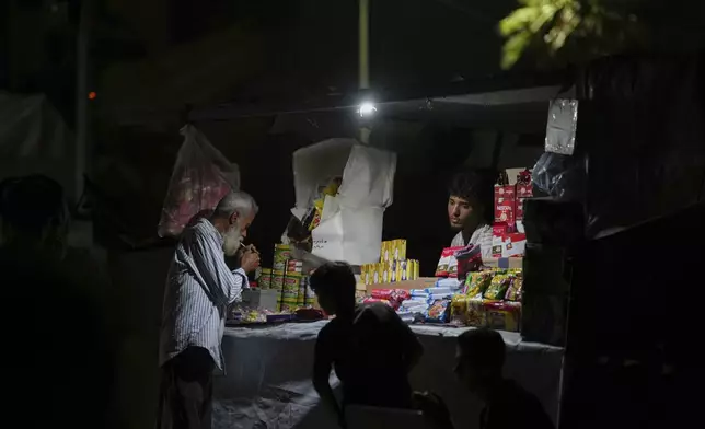 A Palestinian man lights a cigarette as a street vendor looks on at his stand near the beachfront at a tent camp for displaced people in the Gaza City port, Tuesday, Sept. 2, 2025. (AP Photo/Jehad Alshrafi)