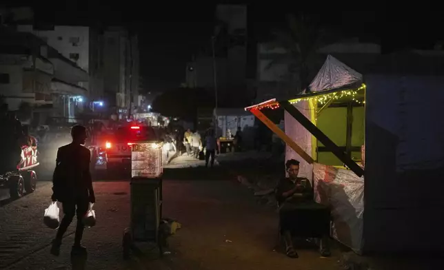 A Palestinian man looks at his phone as he sits next to a makeshift shop on a street in the Gaza City, Tuesday, Sept. 2, 2025. (AP Photo/Jehad Alshrafi)