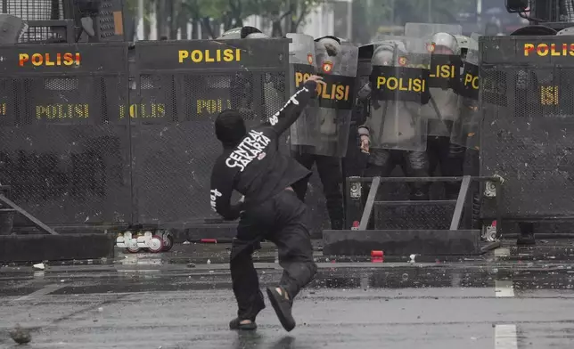 Police officers cover themselves with riot shields as a protester throws rock at them during a protest against lavish allowances given to parliament members, outside the parliament in Jakarta, Indonesia, Sunday, Aug. 31, 2025. (AP Photo/Dita Alangkara)