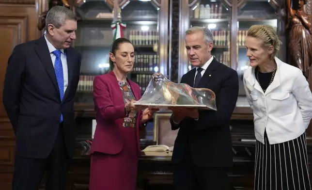 Jesus Maria Tarriba, left, and Diana Fox Carney, right, look on as Mexican President Claudia Sheinbaum presents a gift to Canada's Prime Minister Mark Carney at the National Palace in Mexico City, Thursday, Sept. 18, 2025. (Adrian Wyld/The Canadian Press via AP)