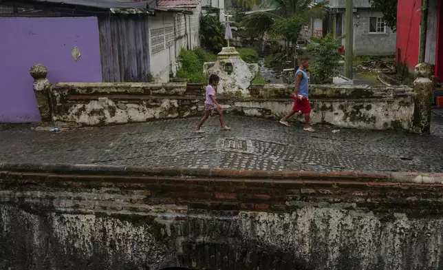 Residents cross a colonial-era bridge in Portobelo, a town on Panama's Caribbean coast that was once a key port where Spanish treasure fleets loaded silver and gold for shipment to Europe, Thursday, Aug. 14, 2025. (AP Photo/Matias Delacroix)