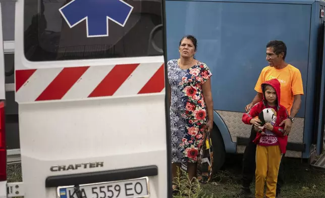A family stays near an ambulance during the evacuation from the village of Yarova, that was hit by Russian aerial strike, which killed dozens of civilians, in Sloviansk, Donetsk region, Tuesday, Sept.9, 2025. (AP Photo/Alex Babenko)