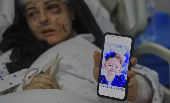 Amani Bazzi, who was injured Sunday in the town of Bint Jbeil, shows a portrait of one her three kids who were killed after an Israeli drone strike hit her family car, as she lies in Tibnin hospital, southern Lebanon, Monday, Sept. 22, 2025. (AP Photo/Mohammed Zaatari)