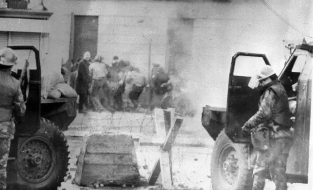 Soldiers take cover behind their sandbagged armoured cars while dispersing rioters with CS gas in Londonderry, Northern Ireland, on Jan. 1, 1972. (PA via AP)