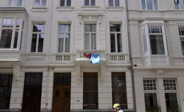 A cyclist looks up at a Palestinian and World Peace flag displayed from a balcony of a house in Antwerp, Belgium, Tuesday, Sept. 2, 2025. (AP Photo/Virginia Mayo)