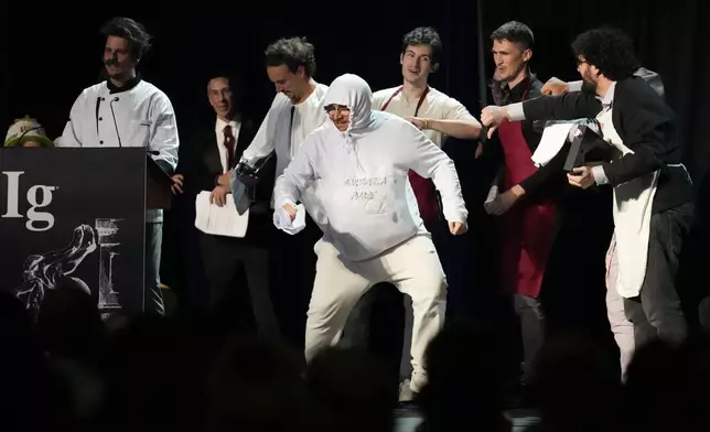 The Ig Nobel Prize for nutrition is accepted by Daniele Dendi, Gabriel H. Segniagbeto, Roger Meek, and Luca Luiselli, for studying the extent to which a certain kind of lizard chooses to eat certain kinds of pizza, Thursday, Sept. 18, 2025, in Boston. (AP Photo/Robert F. Bukaty)