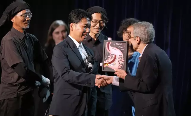 The Ig Nobel Prize for biology is accepted by Tomoki Kojima, Kazato Oishi, Yasushi Matsubara, Yuki Uchiyama, Yoshihiko Fukushima, Naoto Aoki, Say Sato, Tatsuaki Masuda, Junichi Ueda, Hiroyuki Hirooka, and Katsutoshi Kino, for their experiments to learn whether cows painted with zebra- like striping can avoid being bitten by flies, Thursday, Sept. 18, 2025, in Boston. (AP Photo/Robert F. Bukaty)