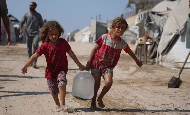 Displaced Palestinians girls carry a jerrycan after collecting water from a distribution point at a tent camp in Muwasi, an area that Israel has designated as a safe zone, in Khan Younis southern Gaza Strip, Monday, Sept. 29, 2025. (AP Photo/Jehad Alshrafi)