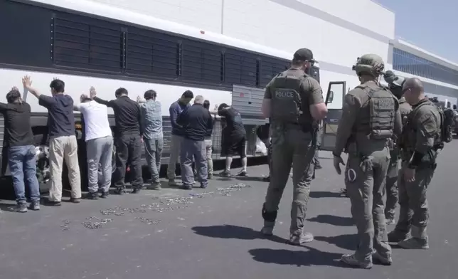This image from video provided by U.S. Immigration and Customs Enforcement via DVIDS shows manufacturing plant employees waiting to have their legs shackled at the Hyundai Motor Group’s electric vehicle plant, Thursday, Sept. 4, 2025, in Ellabell, Ga. (Corey Bullard/U.S. Immigration and Customs Enforcement via AP)