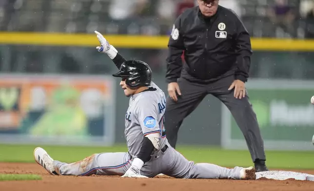 Miami Marlins' Javier Sanoja gestures to the dugout after reaching seocnd bse on an RBI double off Colorado Rockies starting pitcher Kyle Freeland as second base umpire Doug Eddings looks on in the sixth inning of a baseball game Tuesday, Sept. 16, 2025, in Denver. (AP Photo/David Zalubowski)